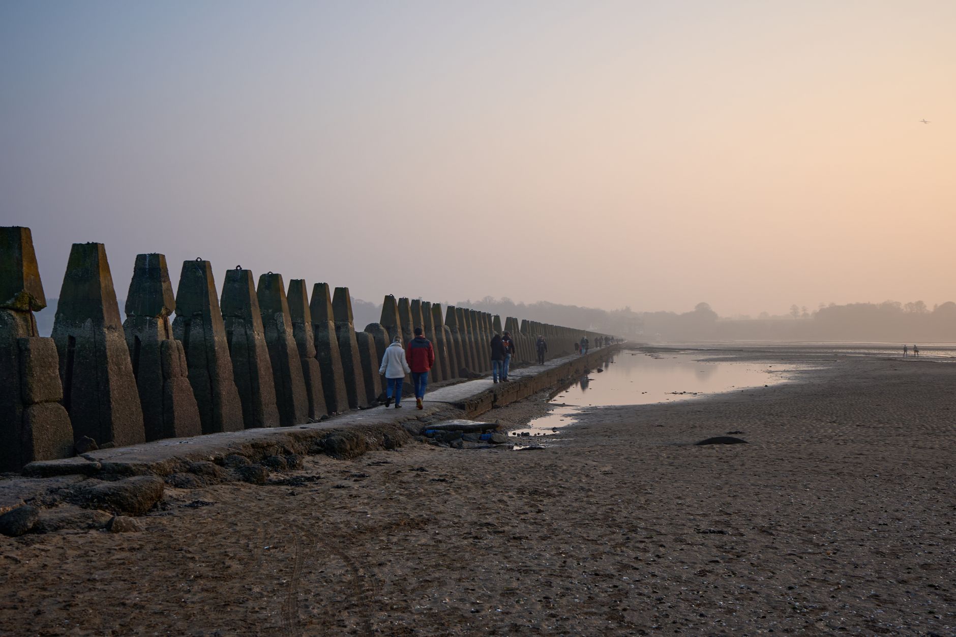 Walkers on the Cramond causeway beside the wartime pylons at sunset with the tide out