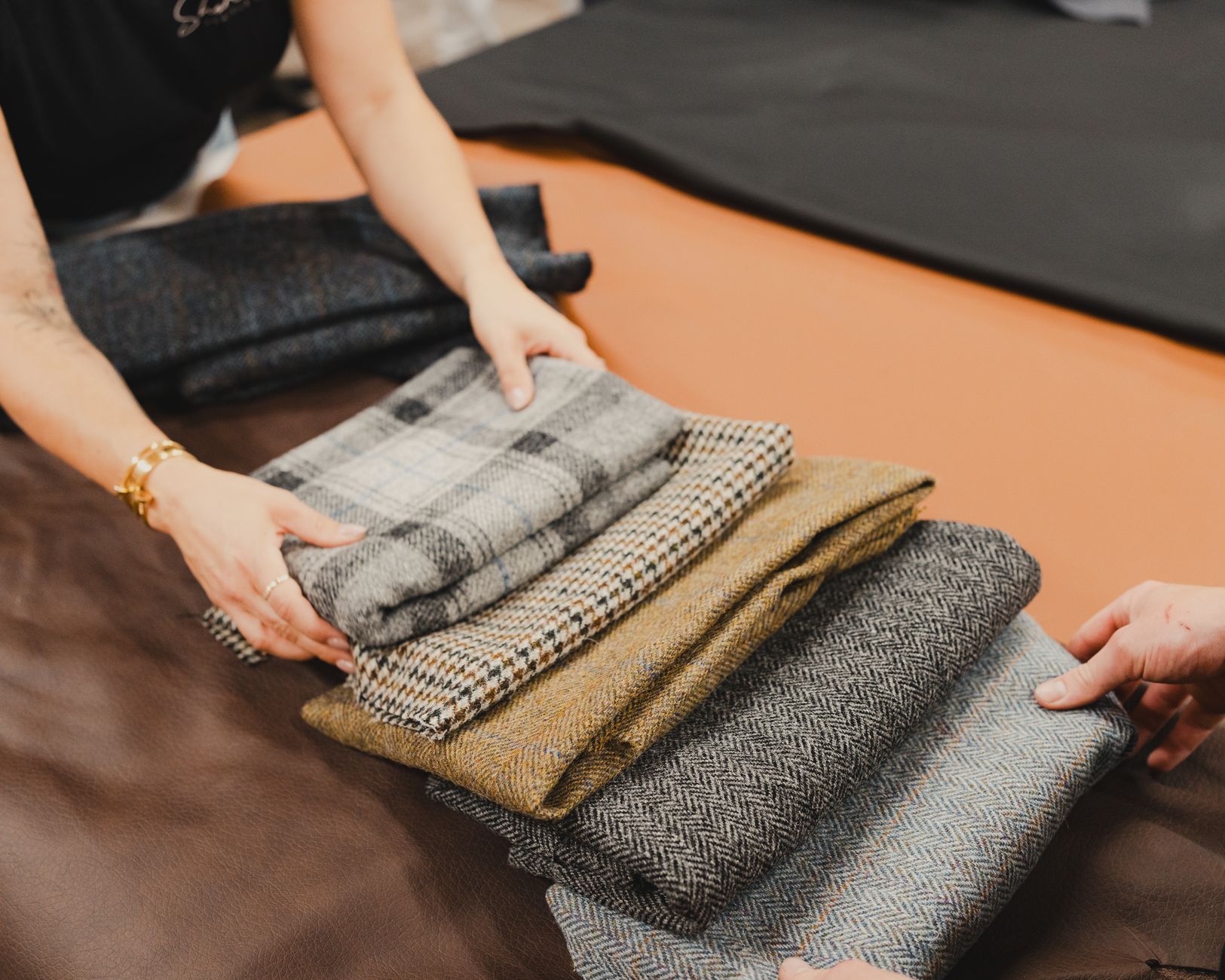 Hands folding checked and herringbone tweed fabrics in a tailor's shop