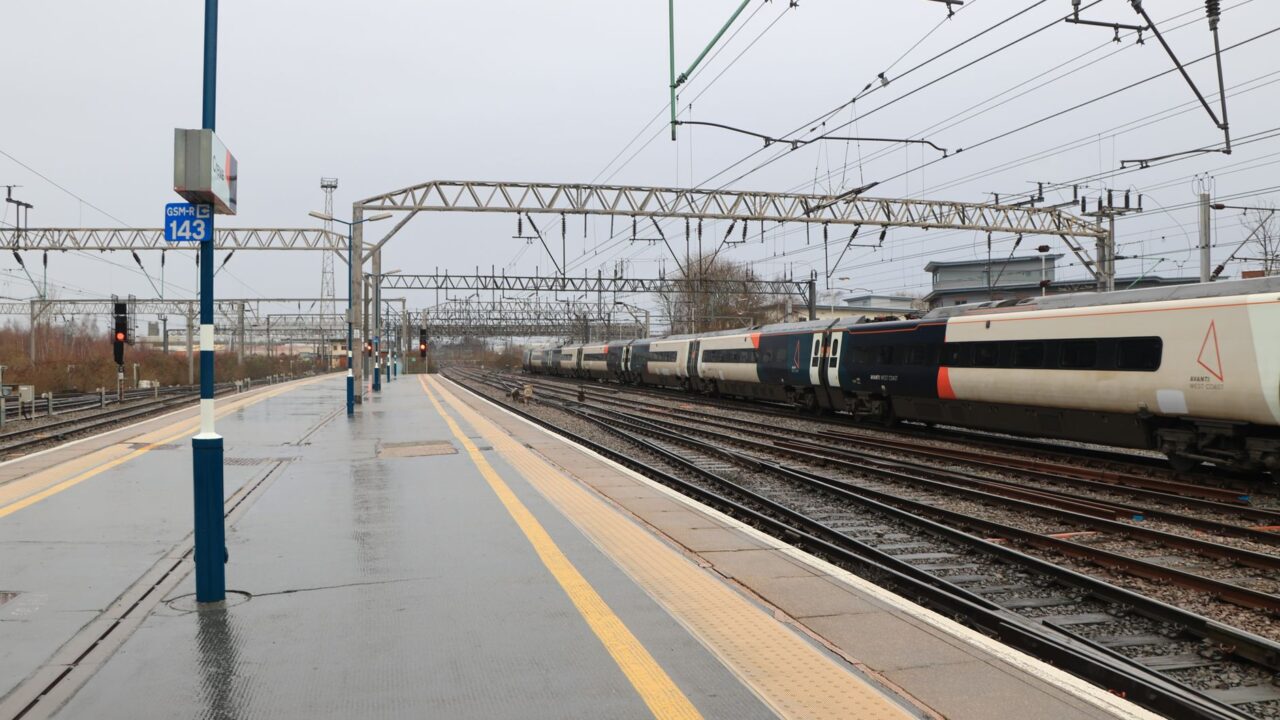 An intercity train pulling into a rain-soaked British station platform under overhead electric wires
