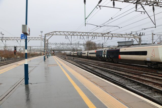 An intercity train pulling into a rain-soaked British station platform under overhead electric wires