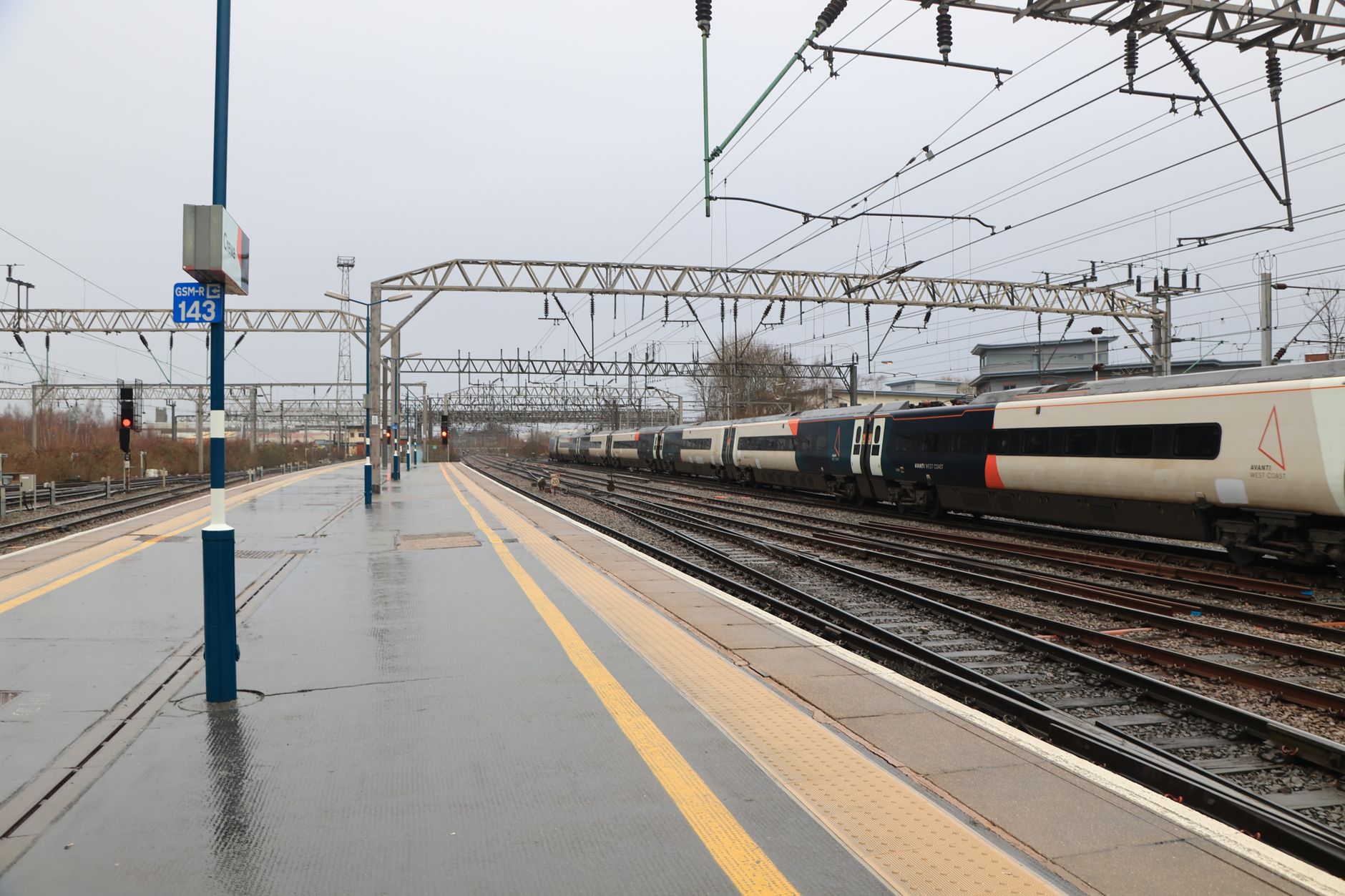 An intercity train pulling into a rain-soaked British station platform under overhead electric wires