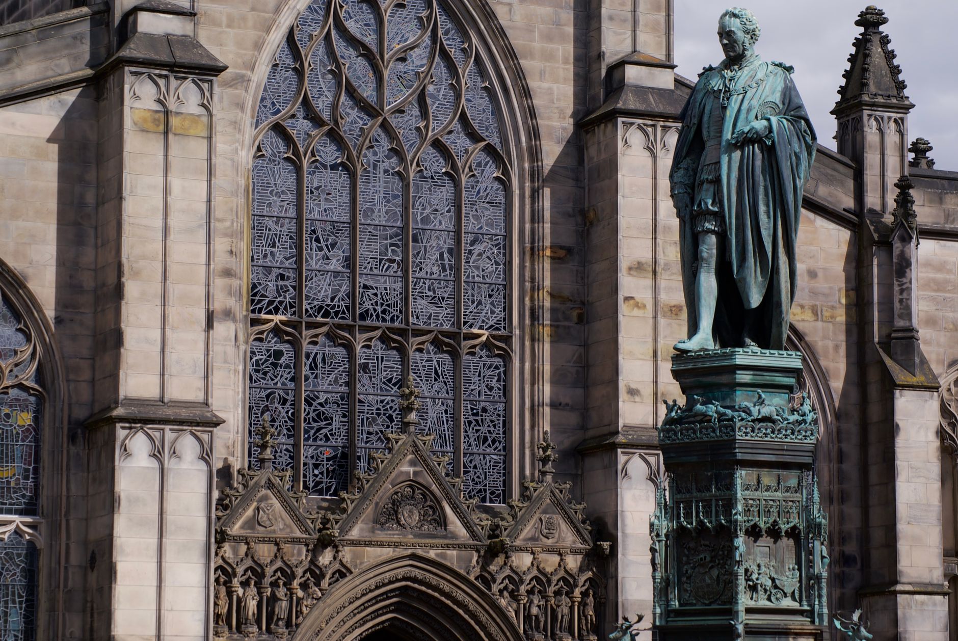 Gothic tracery window and a bronze statue outside St Giles Cathedral in Edinburgh