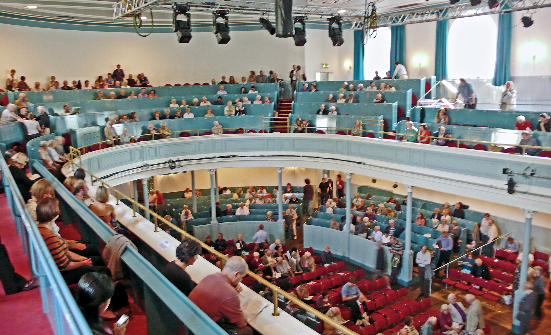 Audience members fill red seats beneath the curved blue balcony inside the Queen's Hall in Edinburgh.