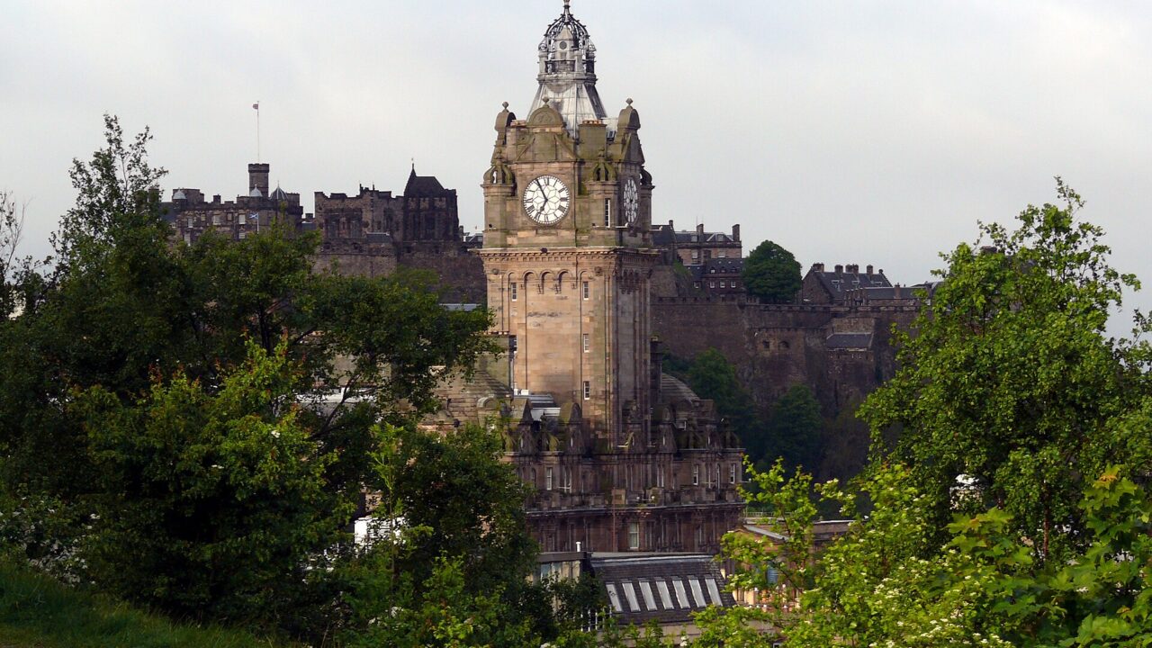 The Balmoral clock tower and Edinburgh Castle rise above leafy trees in a view from Calton Hill, Edinburgh.