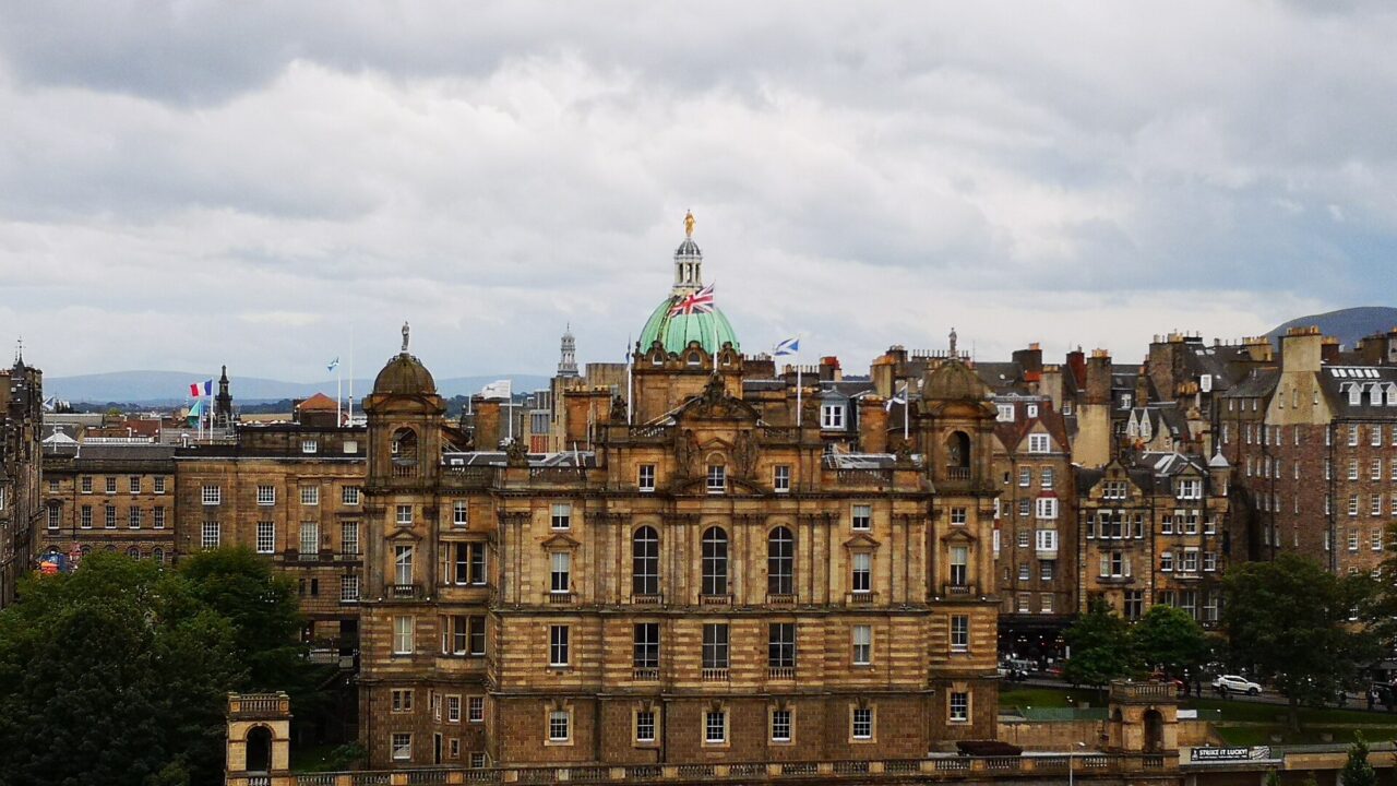 The Bank of Scotland headquarters in Edinburgh rises above trees, with a green central dome and ornate sandstone facade.