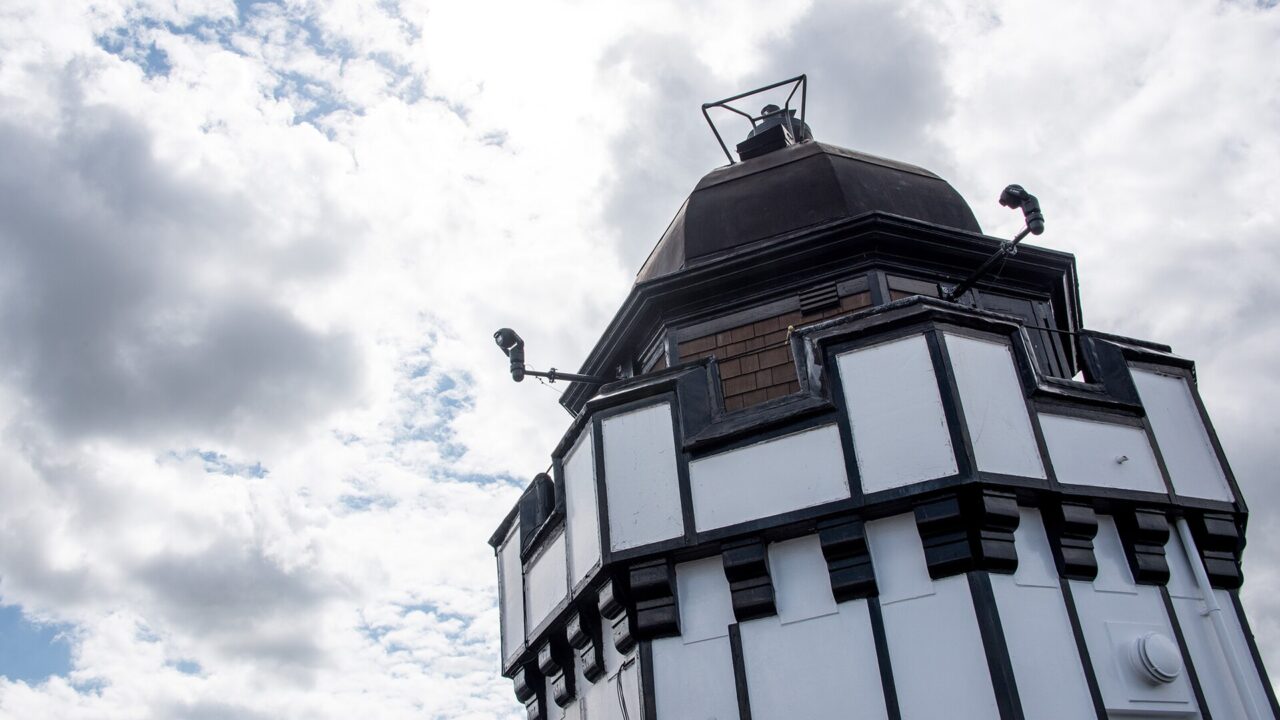 The black-and-white rooftop tower and dark dome of Camera Obscura in Edinburgh rise against a cloudy sky.