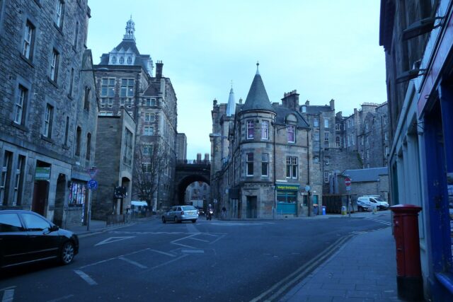 Budget Backpackers occupies a turreted stone corner building beside a bridge in Edinburgh's Old Town, with cars at the junction.