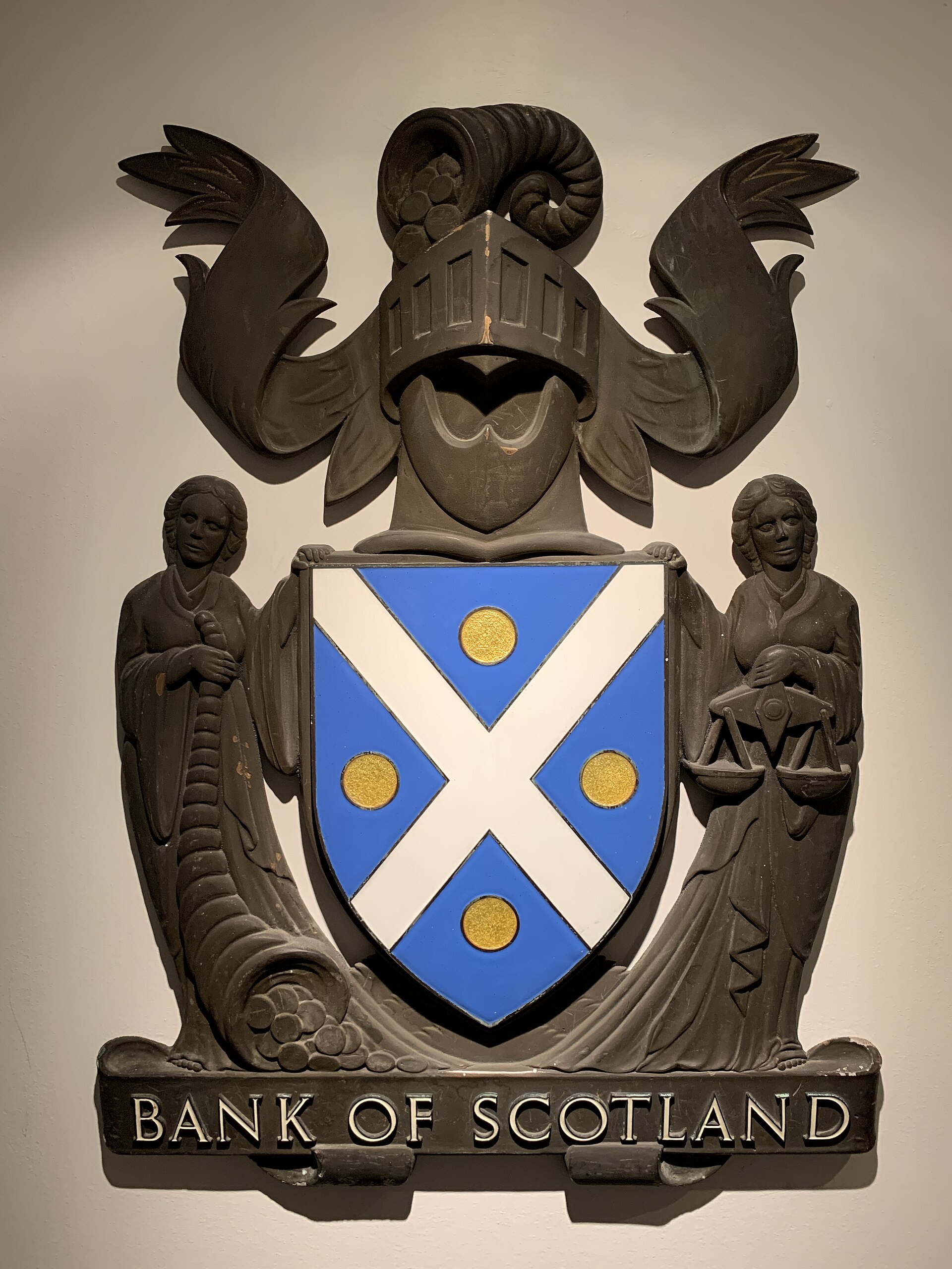 A carved Bank of Scotland emblem with a blue saltire shield and supporting figures at Edinburgh's Museum on the Mound.