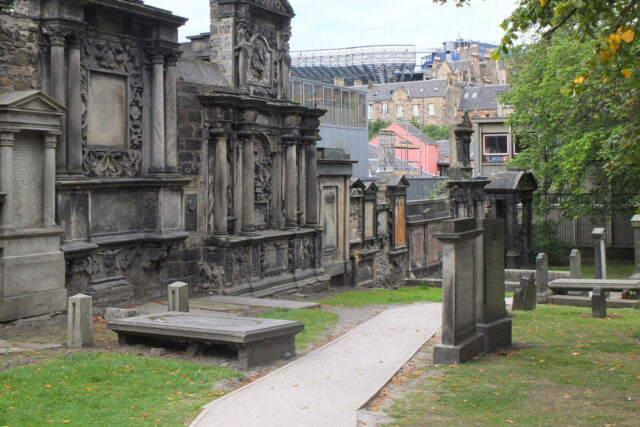 Carved mural monuments line a path between table tombs and upright gravestones in Greyfriars Kirkyard, Edinburgh.