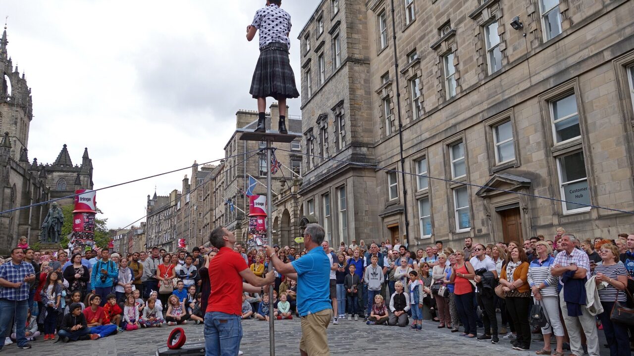 A crowd watches a street performer high above the cobbled Royal Mile, surrounded by Edinburgh's tall stone buildings.
