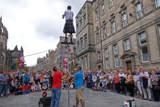 A crowd watches a street performer high above the cobbled Royal Mile, surrounded by Edinburgh's tall stone buildings.