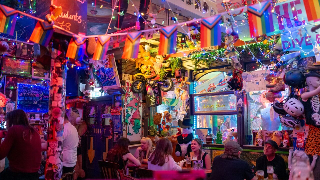 Customers gather beneath colourful flags, fairy lights and hanging toys inside The Dog House bar in Edinburgh.