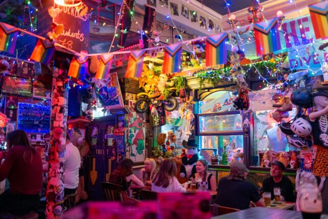 Customers gather beneath colourful flags, fairy lights and hanging toys inside The Dog House bar in Edinburgh.