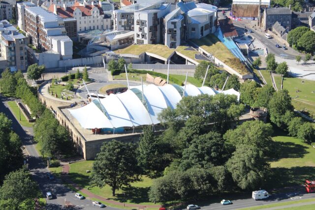 Dynamic Earth in Edinburgh seen from above, with its white tented roof surrounded by trees and neighbouring buildings.