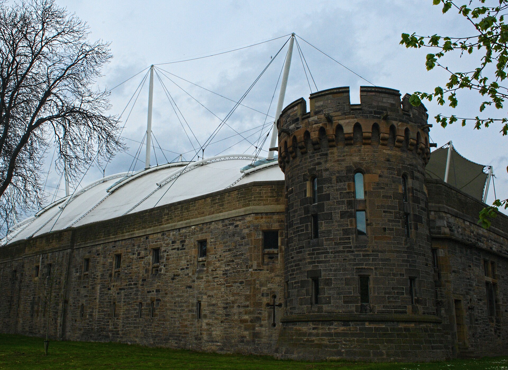 Dynamic Earth's white roof and tall support masts rise above a stone wall and round tower in Edinburgh.