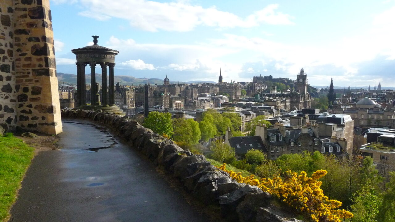 Edinburgh skyline from Calton Hill, with the Dugald Stewart Monument, Balmoral clock tower and castle above sunlit rooftops.