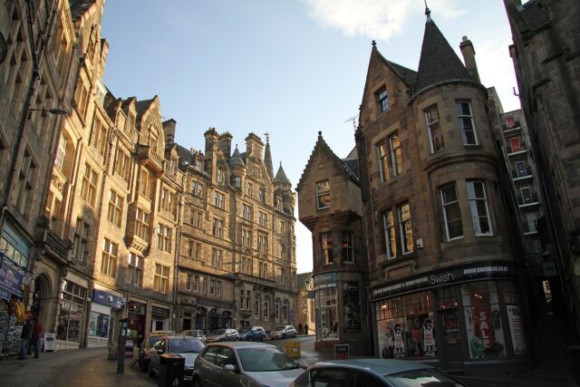 Edinburgh's Cockburn Street curves between tall stone buildings, with stepped gables, a corner turret and shops at street level.