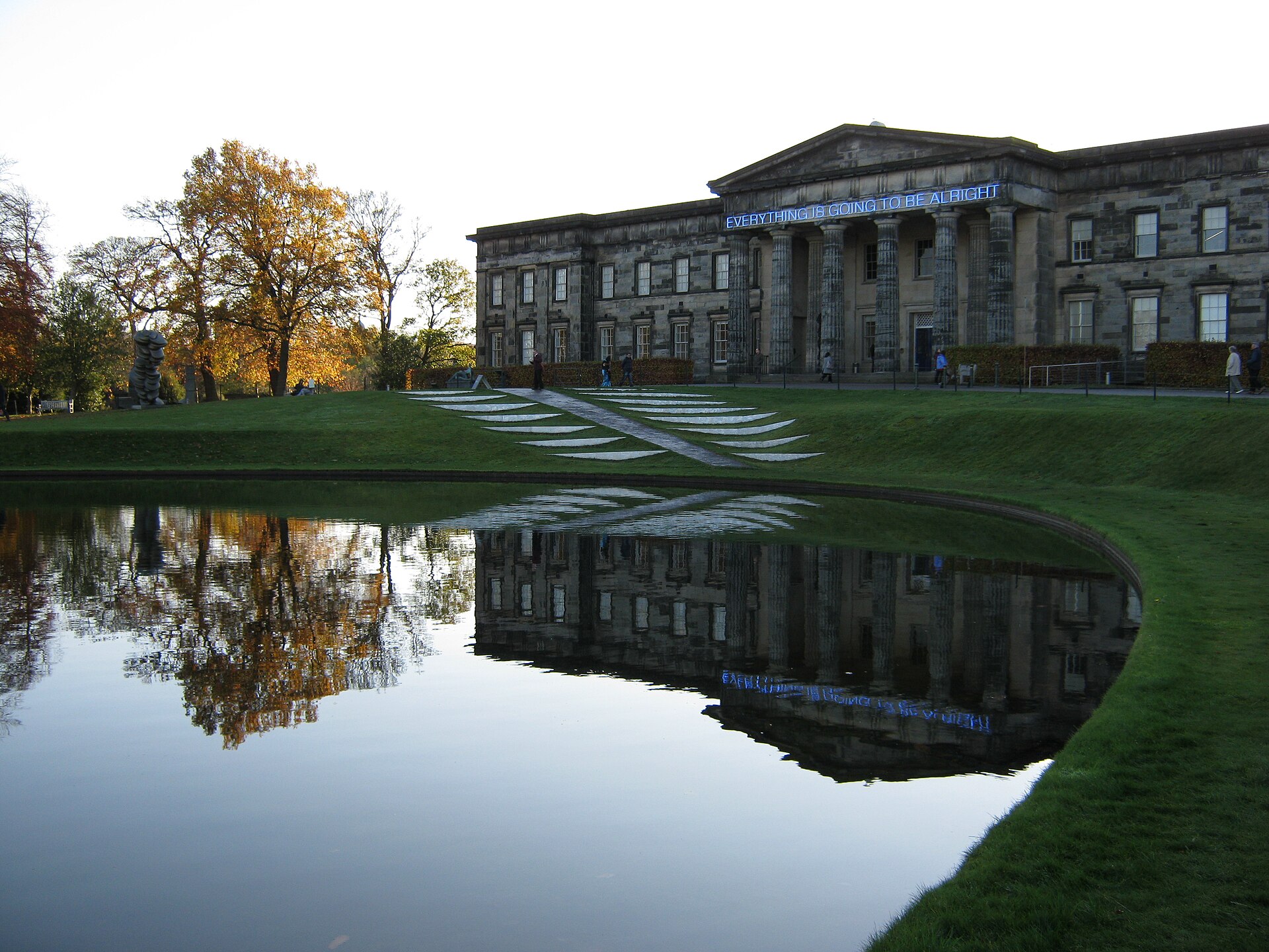 Edinburgh’s Modern One and autumn trees reflect in Landform’s pool beside stepped grass terraces.
