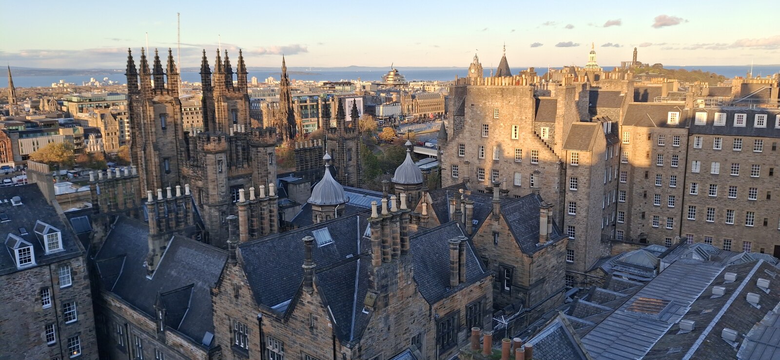 Edinburgh's stone buildings, Gothic pinnacles and slate rooftops spread below Camera Obscura's rooftop, with the Firth of Forth beyond.