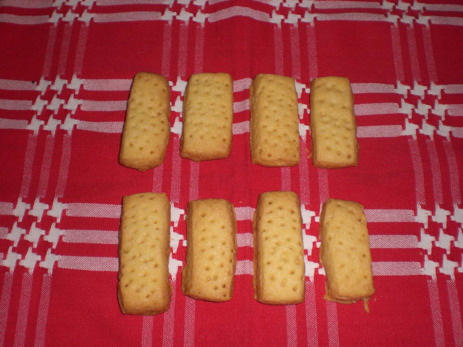 Eight homemade Scottish shortbread fingers with small docking holes are arranged on a red and white checked cloth.