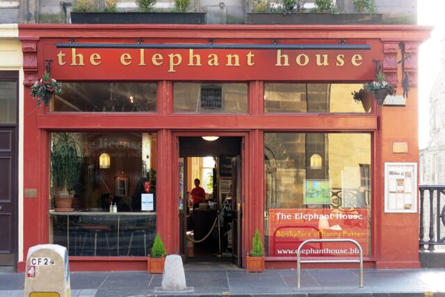 The Elephant House cafe in Edinburgh has a red frontage, gold lettering, hanging baskets and an open central doorway.