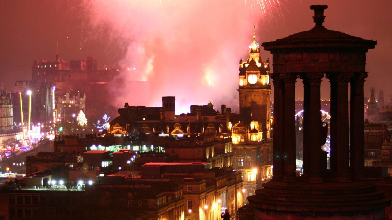 Hogmanay fireworks illuminate Edinburgh Castle beyond the Balmoral clock tower and Calton Hill's Dugald Stewart Monument.