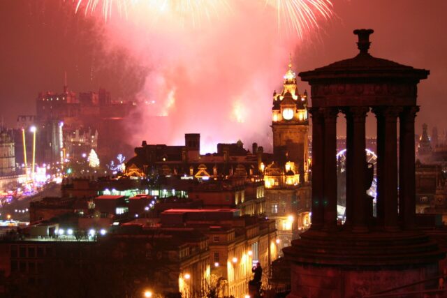 Hogmanay fireworks illuminate Edinburgh Castle beyond the Balmoral clock tower and Calton Hill's Dugald Stewart Monument.