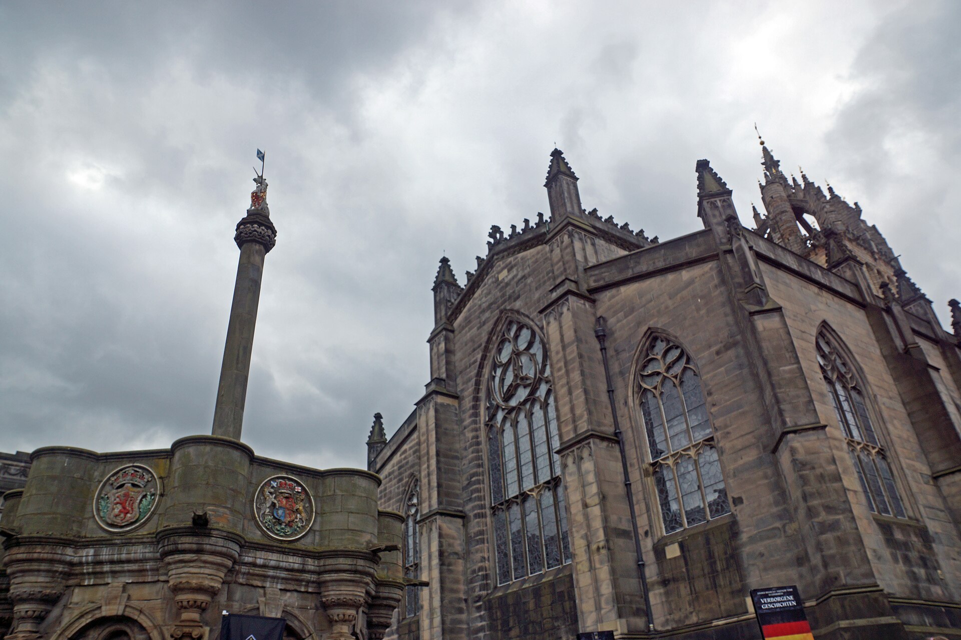 The Mercat Cross stands beside St Giles Cathedral in Edinburgh, beneath its stone crown steeple and cloudy skies.