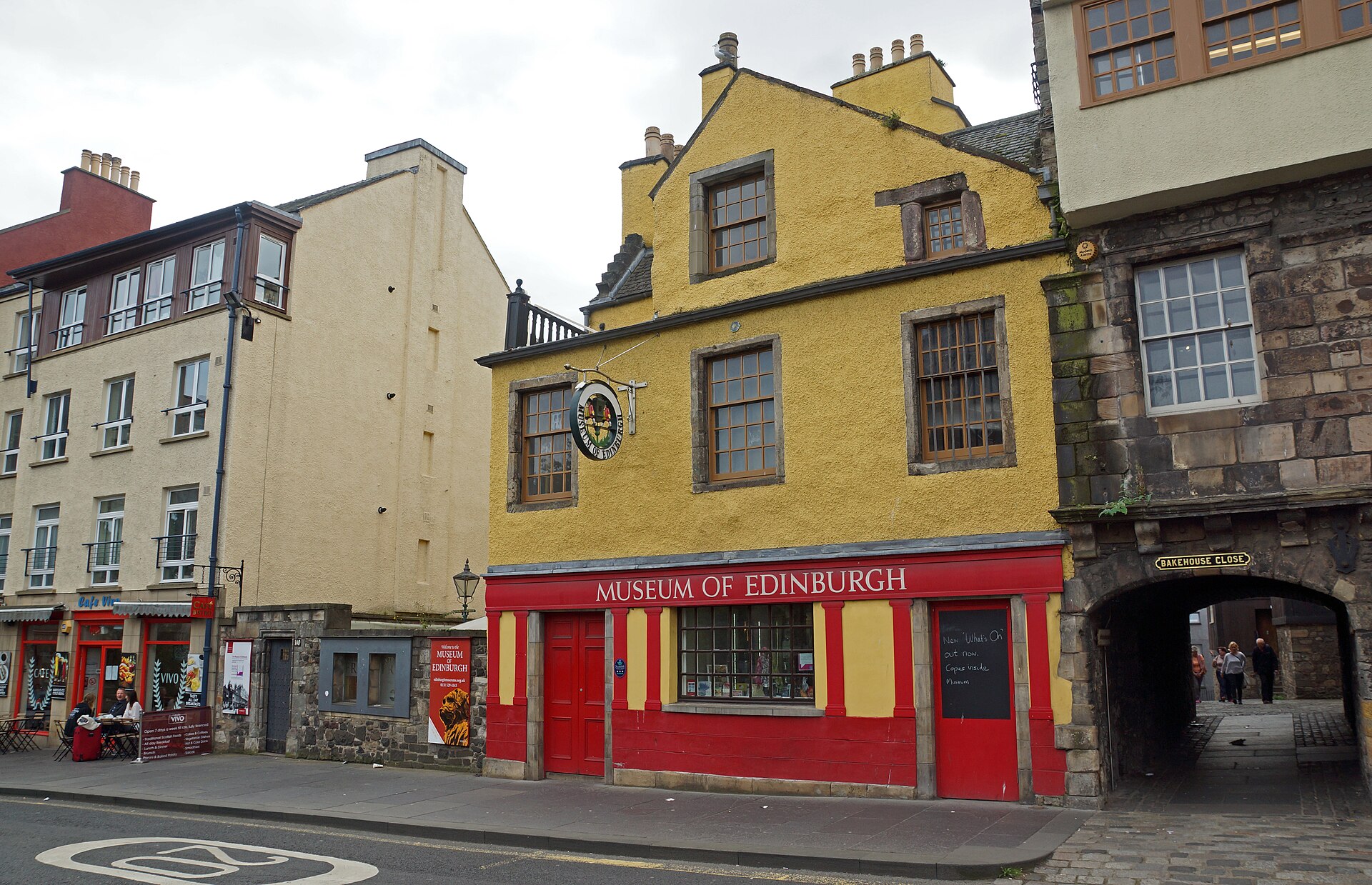 The Museum of Edinburgh on the Royal Mile has a yellow gabled facade, red frontage and a neighbouring stone archway.