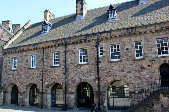 The National War Museum's stone facade at Edinburgh Castle has arched ground-floor openings, white-framed windows and a steep slate roof.