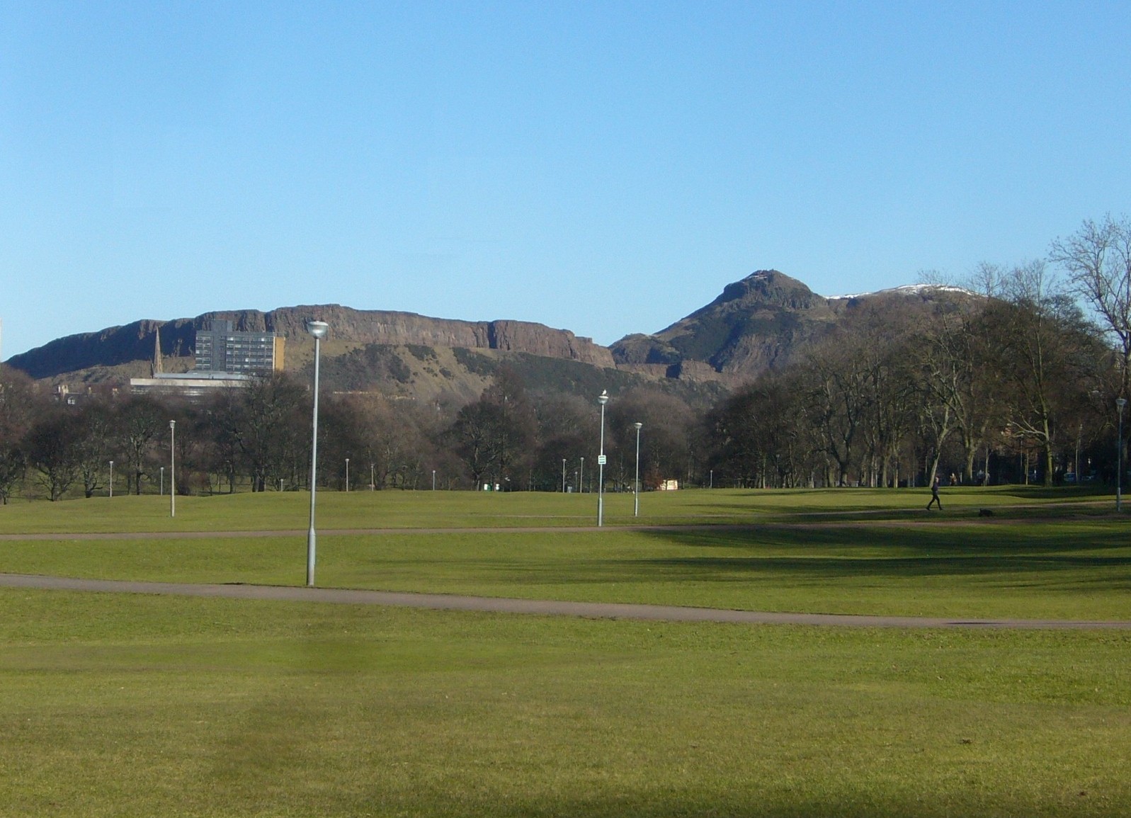 Paths cross the open grass of Bruntsfield Links in Edinburgh, with Arthur's Seat rising beyond a line of trees.
