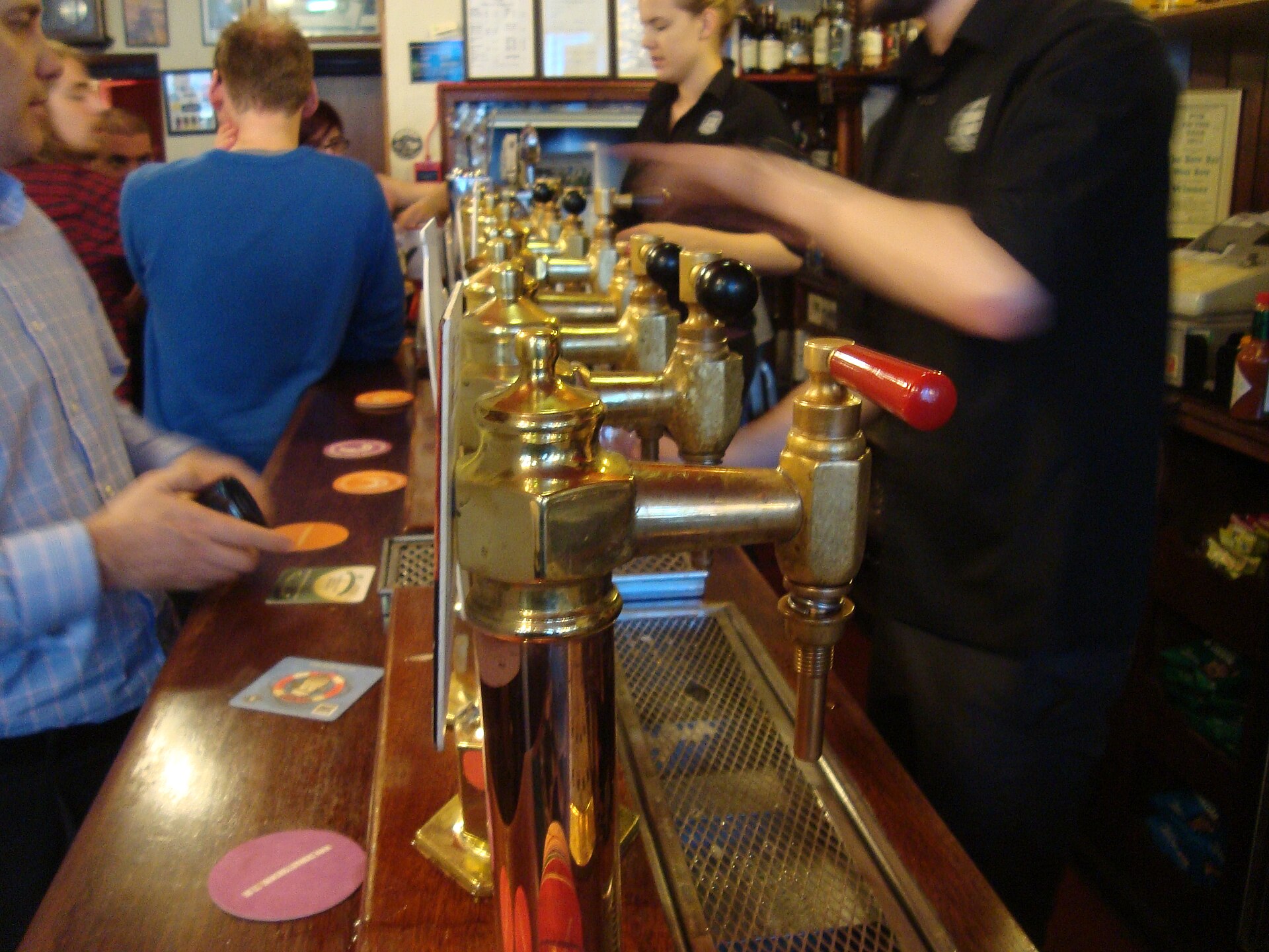Polished brass beer founts line the wooden counter at the Bow Bar in Edinburgh, with staff serving customers.