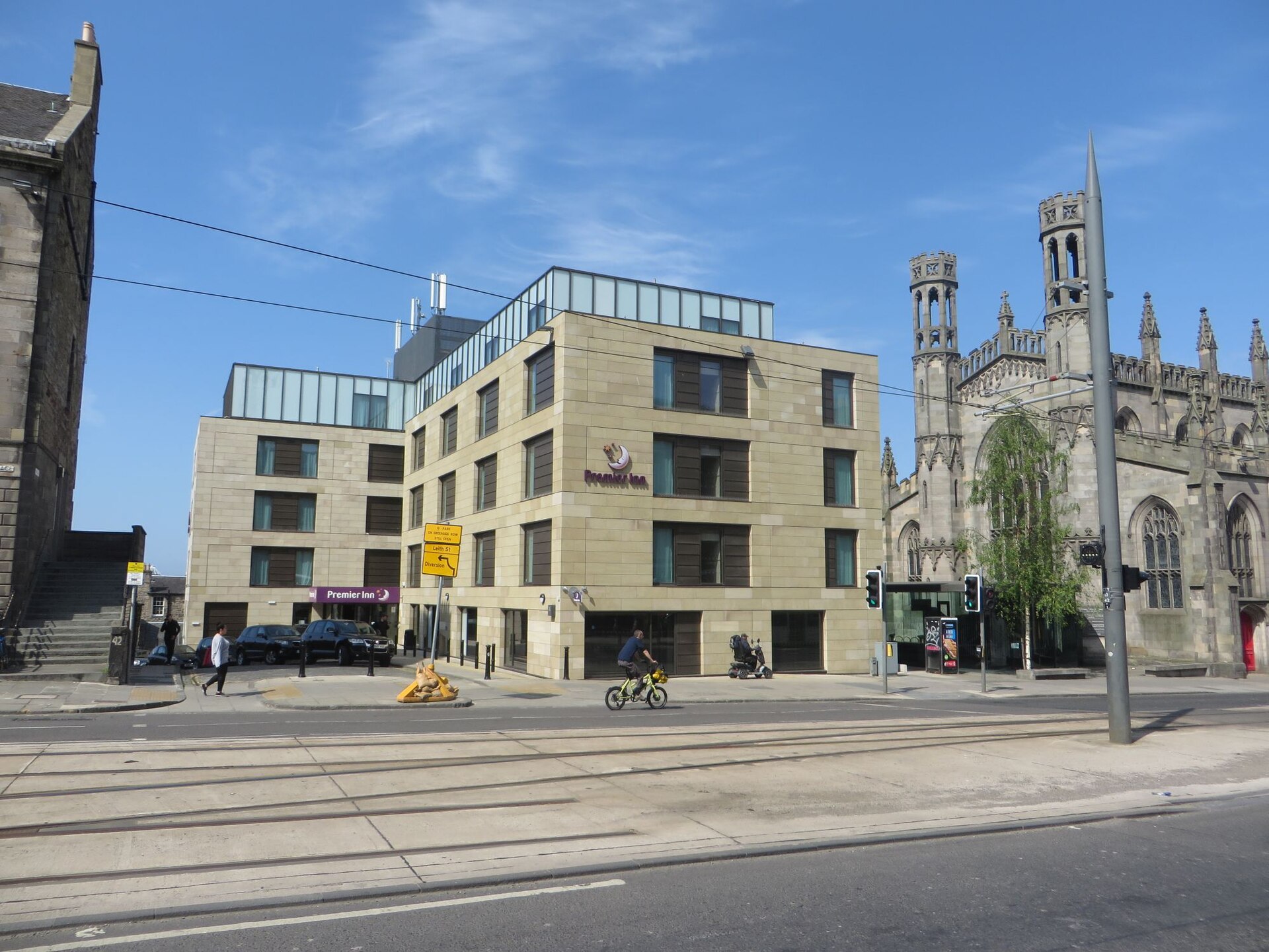 Premier Inn on York Place in Edinburgh stands beside an ornate stone church, with tram tracks and a cyclist in front.