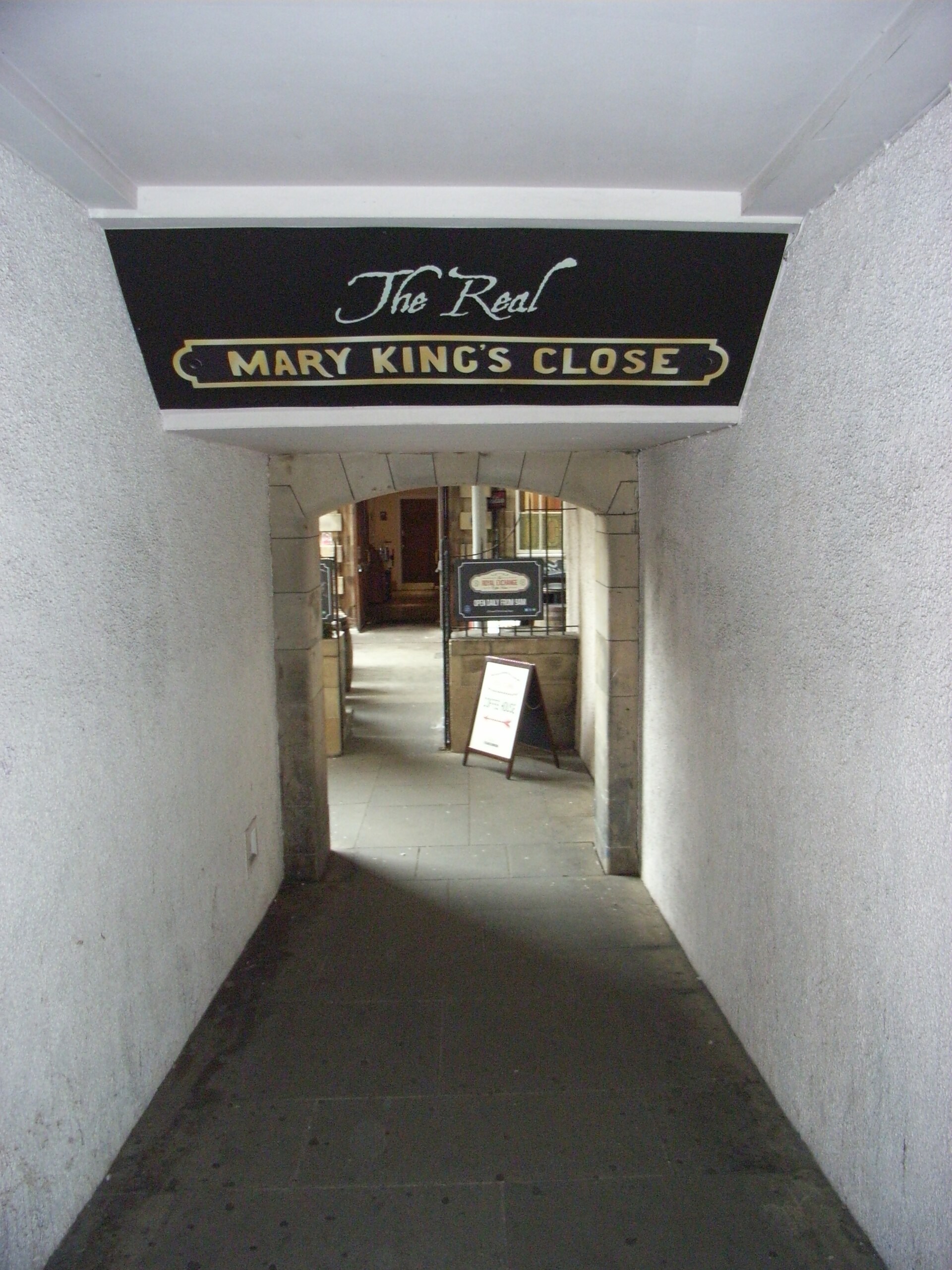 The Real Mary King's Close sign hangs above a covered entrance passage off Edinburgh's Royal Mile, leading toward a stone arch.