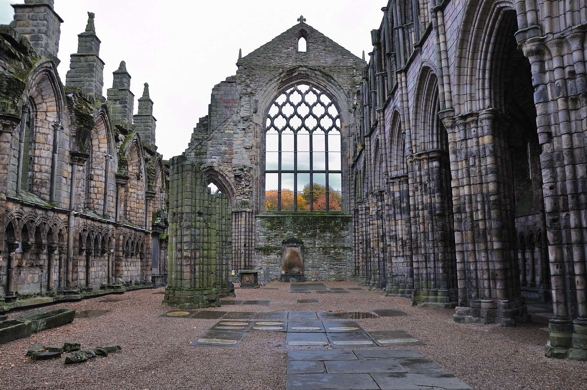 The roofless nave of Holyrood Abbey in Edinburgh, with Gothic arches, a large traceried window and stone floor slabs.