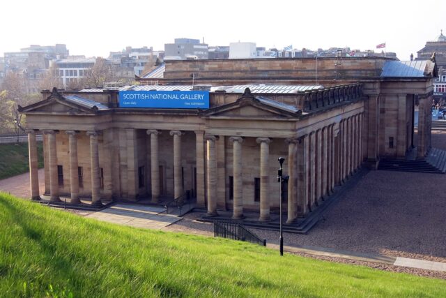 The Scottish National Gallery in Edinburgh, with sandstone columns, twin pediments and a grassy slope in the foreground.