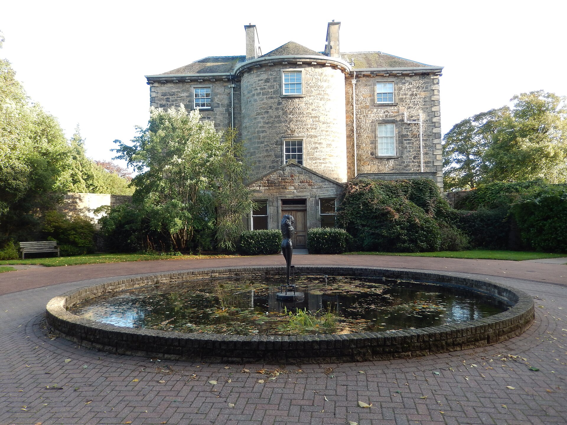 A standing sculpture rises from a circular pool outside Inverleith House in the Royal Botanic Garden Edinburgh.