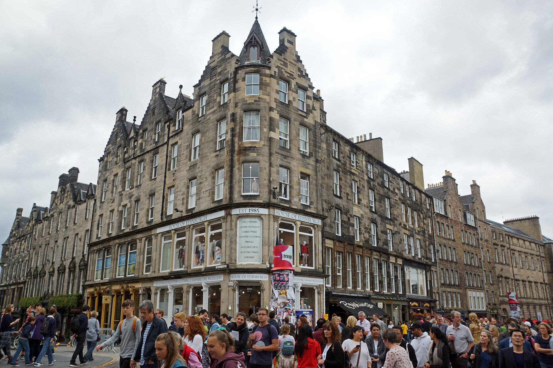 Tall stone buildings and ground-floor shopfronts overlook crowds walking along the Royal Mile in Edinburgh's Old Town.