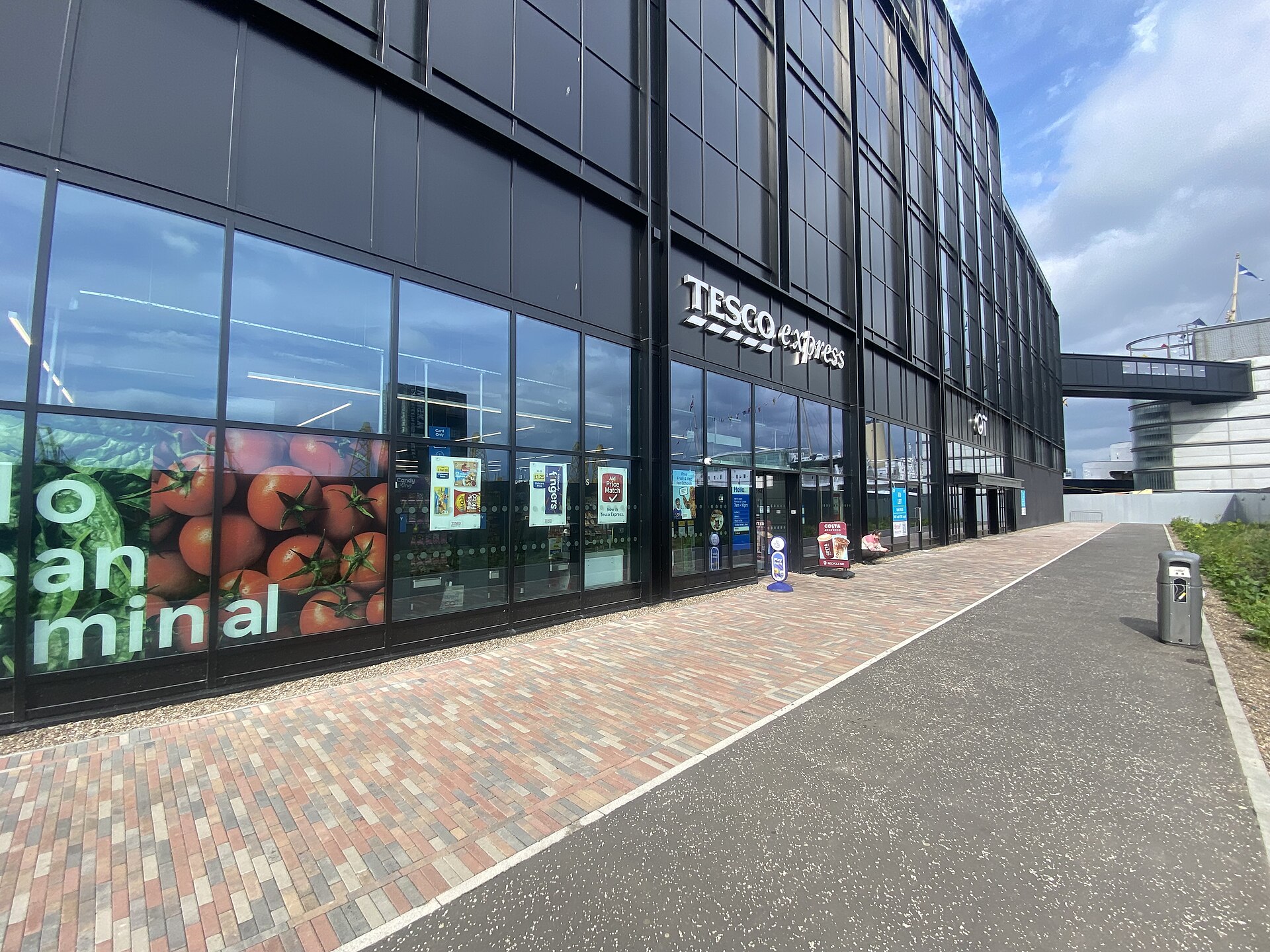 Tesco Express at Edinburgh's Ocean Terminal has a glass storefront beneath dark cladding beside a paved walkway.