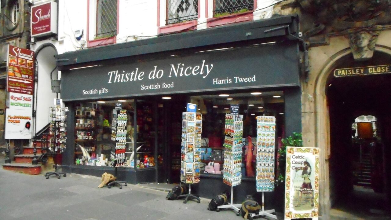 Thistle do Nicely displays postcard racks and souvenirs outside its green-fronted shop beside Paisley Close on Edinburgh's Royal Mile.