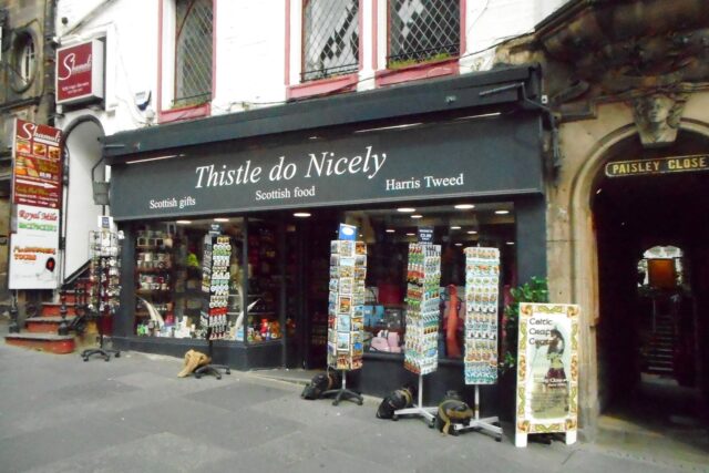 Thistle do Nicely displays postcard racks and souvenirs outside its green-fronted shop beside Paisley Close on Edinburgh's Royal Mile.