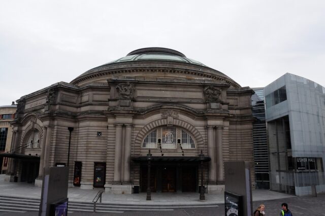 Usher Hall in Edinburgh has an arched stone entrance beneath a broad dome, beside a modern glass extension.