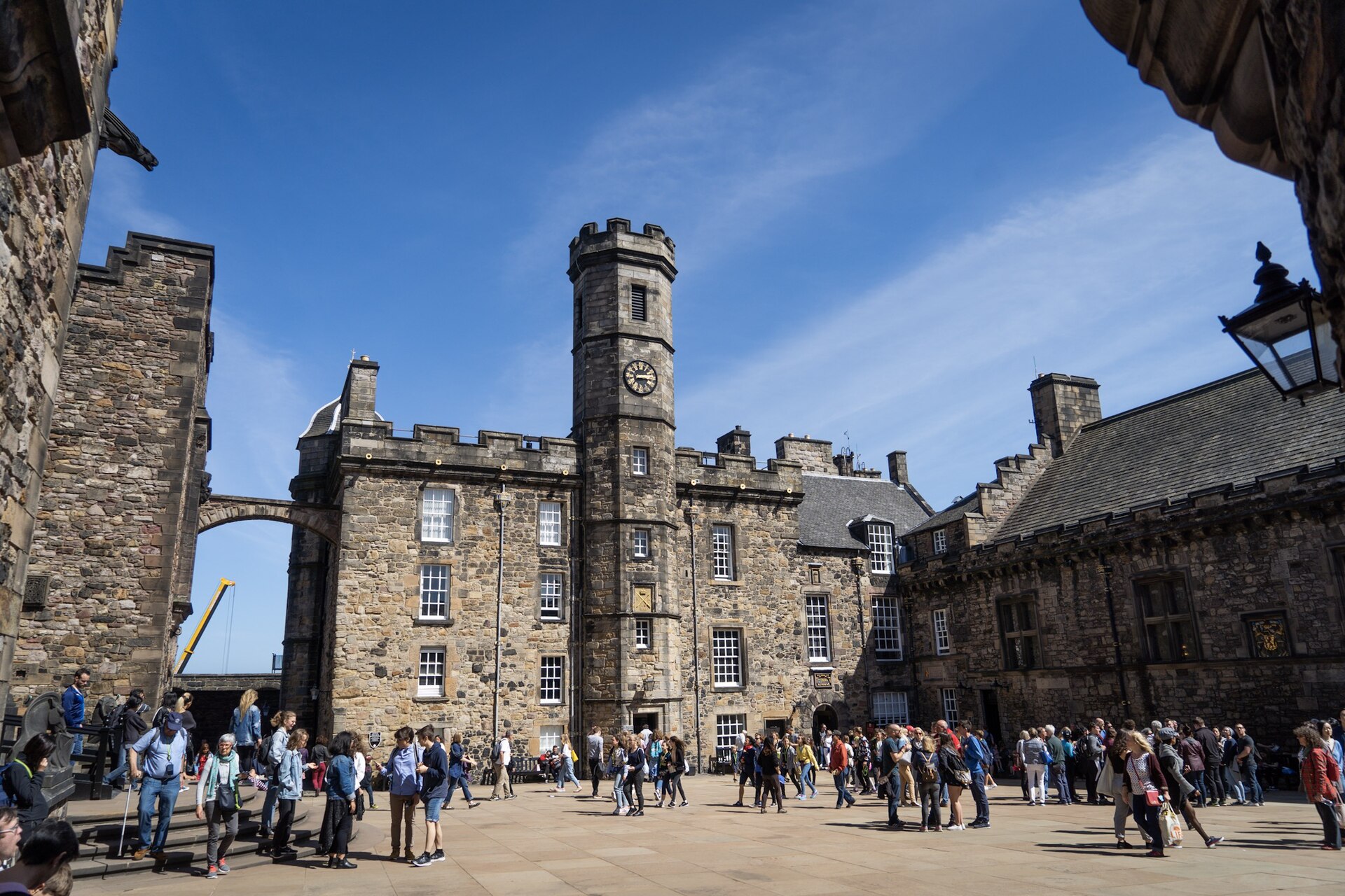 Visitors explore Edinburgh Castle's Crown Square between the Royal Palace clock tower and the stone facade of the Great Hall.