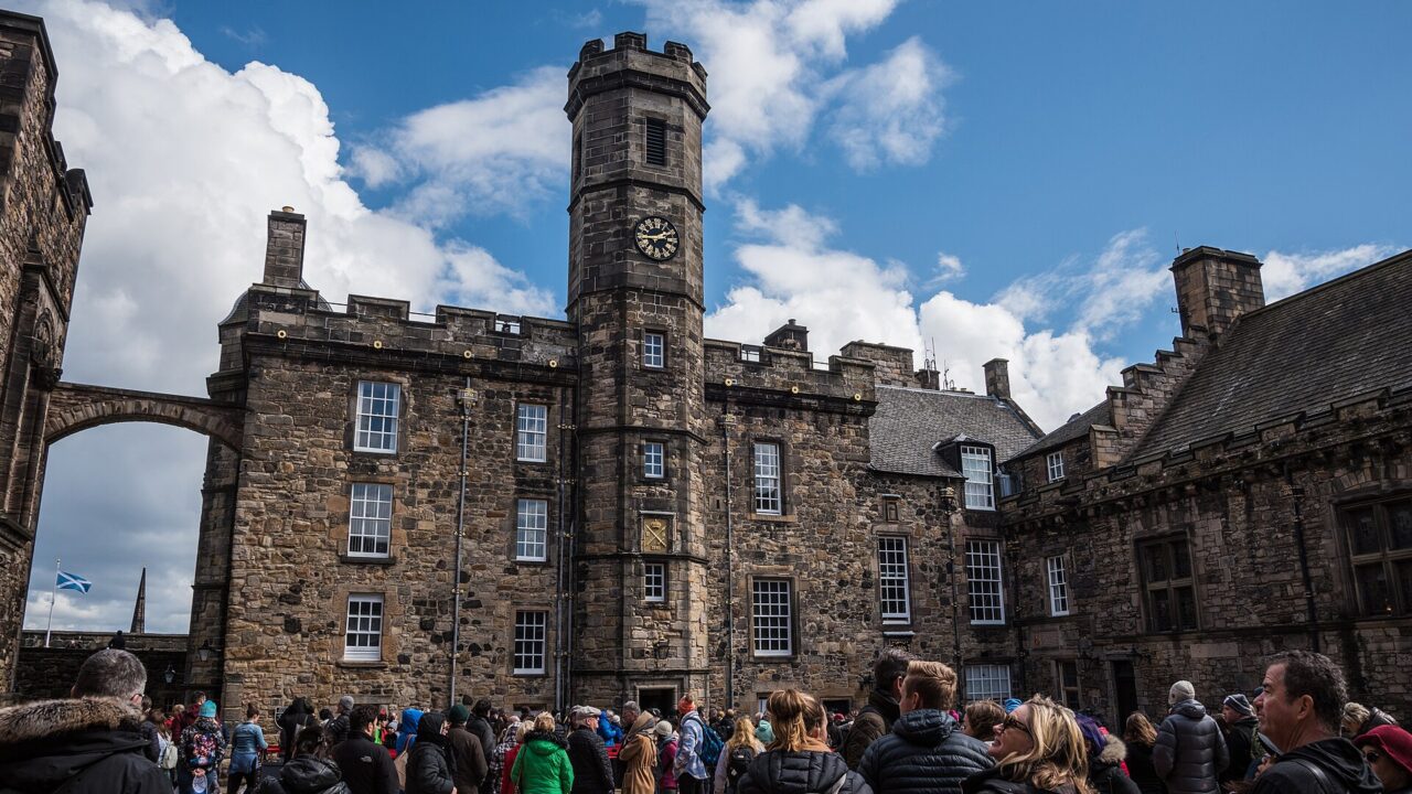 Visitors fill Edinburgh Castle's Crown Square beneath the Royal Palace clock tower, with the Great Hall beside them.