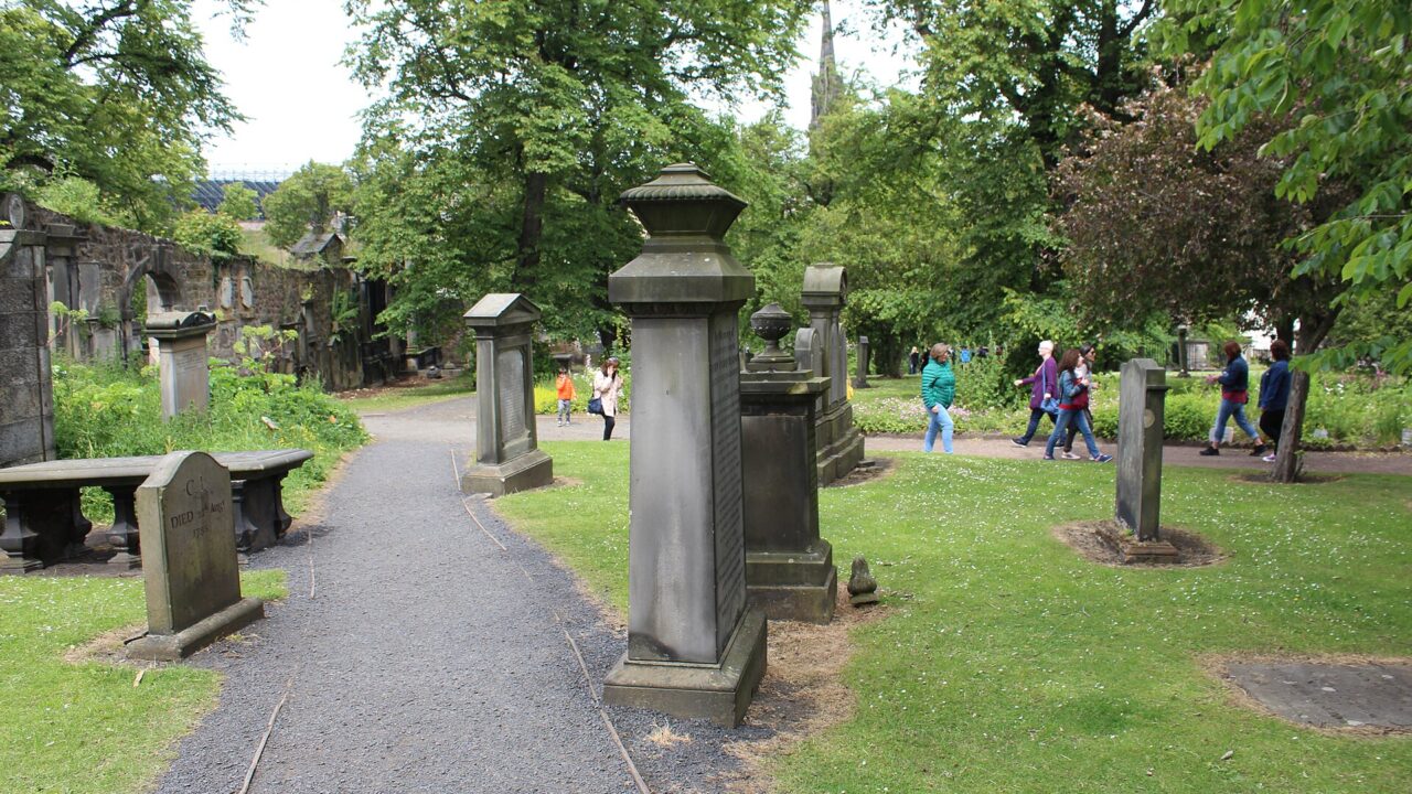 Visitors follow paths between tall gravestones, lawns and leafy trees in Edinburgh's Greyfriars Kirkyard.