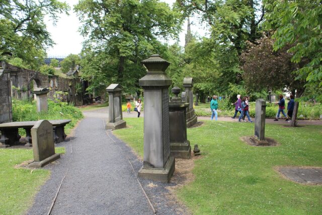 Visitors follow paths between tall gravestones, lawns and leafy trees in Edinburgh's Greyfriars Kirkyard.