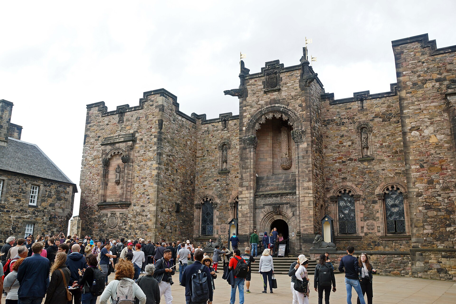 Visitors gather outside the arched entrance and carved stone facade of the Scottish National War Memorial in Edinburgh Castle.