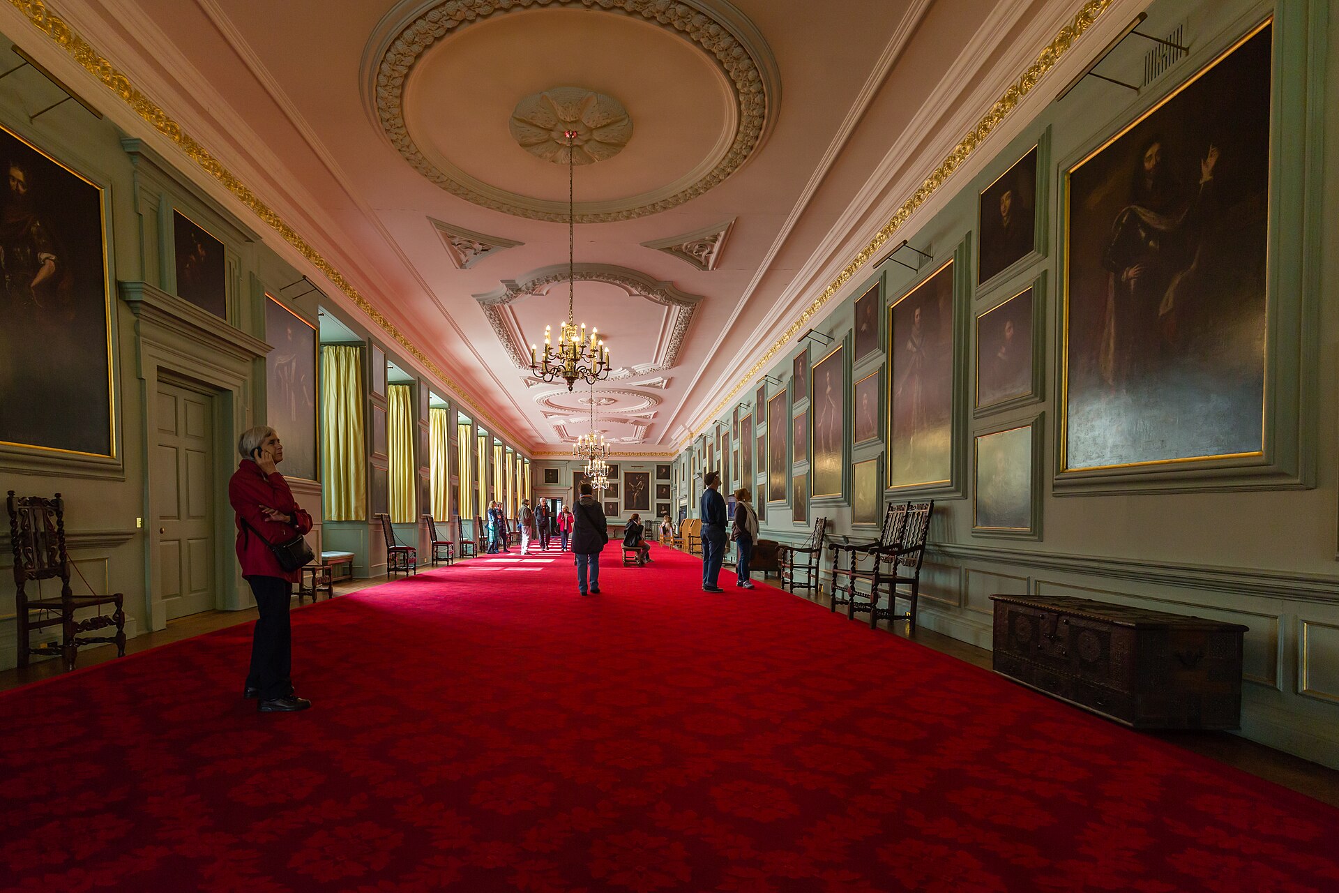 Visitors in the Great Gallery at Edinburgh's Palace of Holyroodhouse, beneath chandeliers and rows of royal portraits.