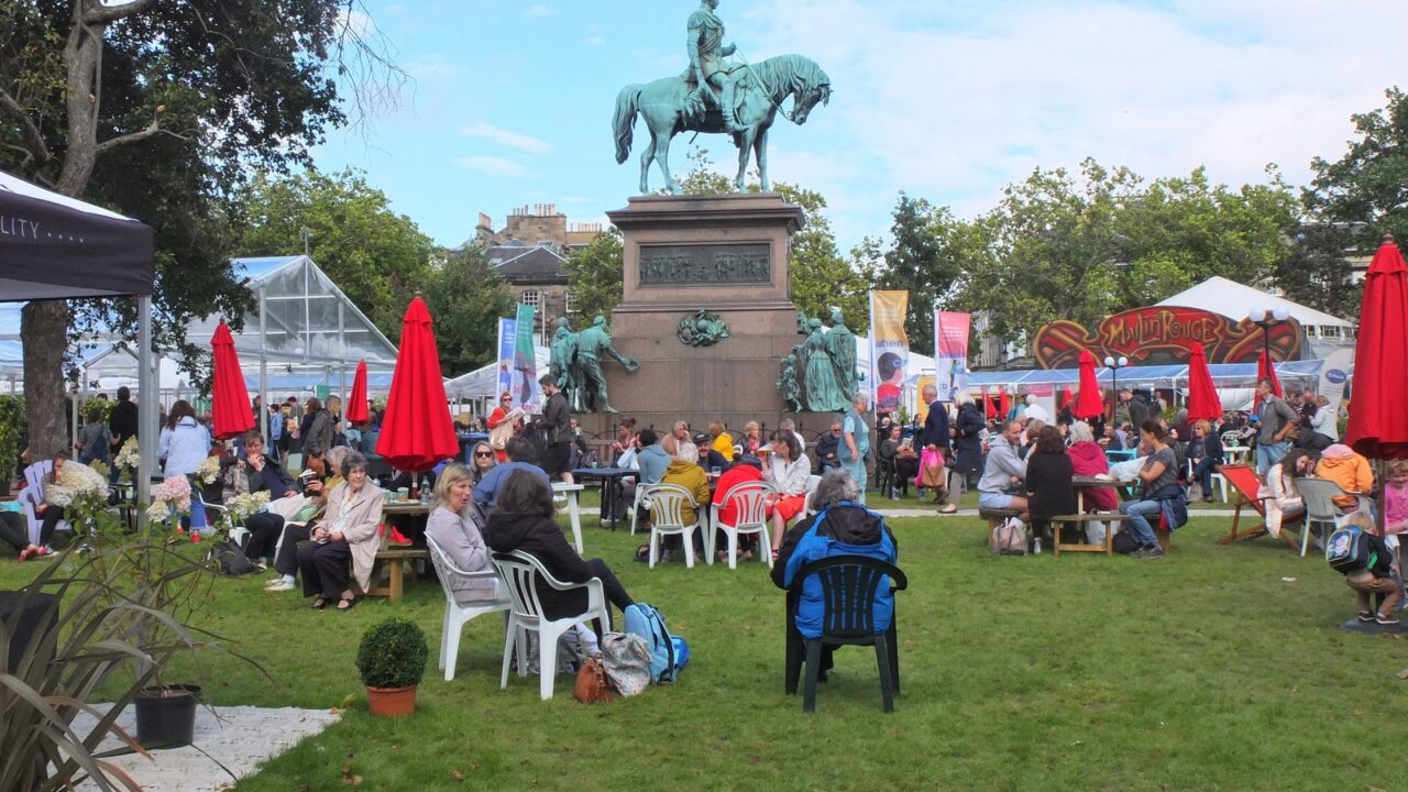 Visitors relax around the equestrian statue among festival tents and red parasols at Edinburgh's Book Festival in Charlotte Square.