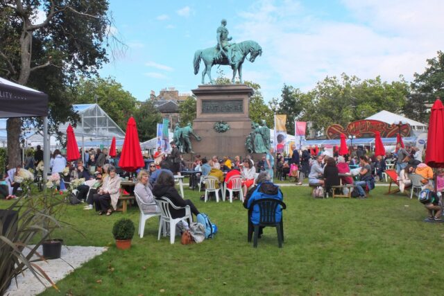 Visitors relax around the equestrian statue among festival tents and red parasols at Edinburgh's Book Festival in Charlotte Square.